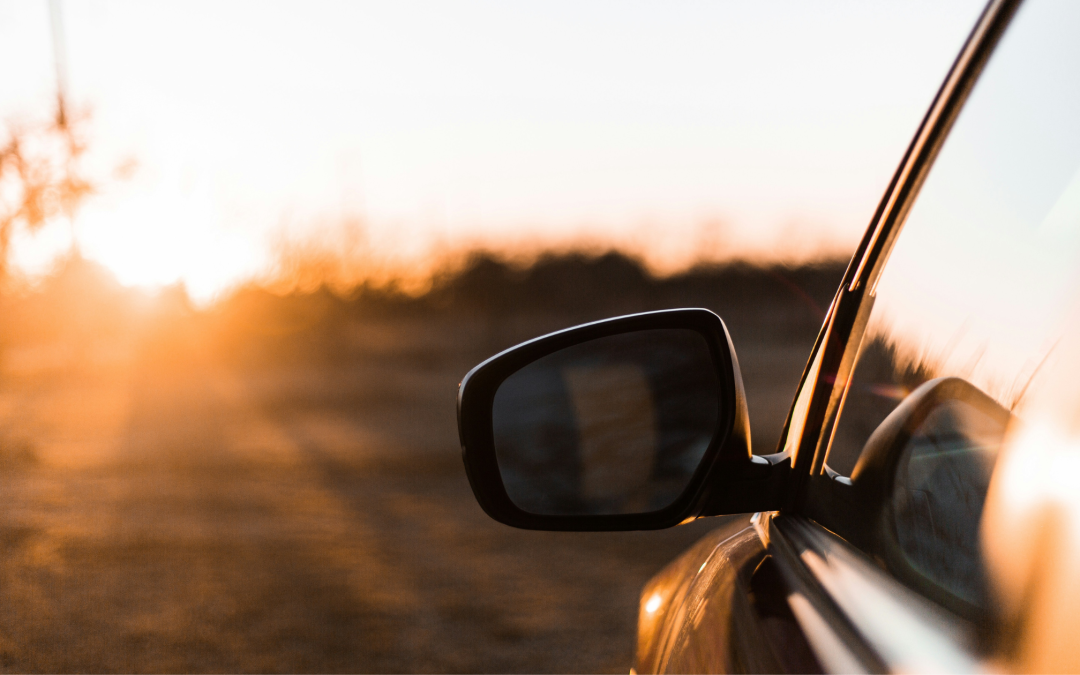 Side view of a car with the side mirror reflecting a road at sunset